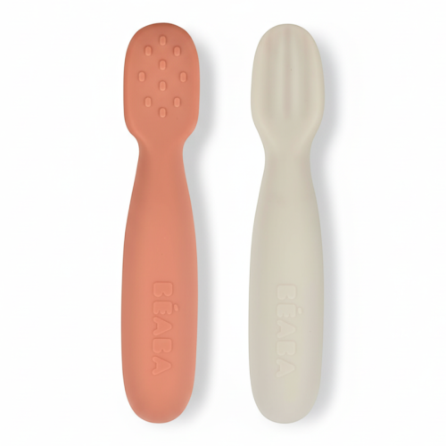Na zdjęciu widać dwie silikonowe łyżeczki-gryzaki Beaba w kolorze terracotta i jasnoszarym. Łyżeczki mają ergonomiczny kształt, zaokrąglone końcówki oraz delikatne wypustki na jednej z nich.